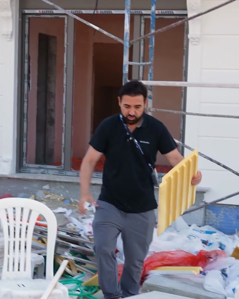 Bărbat transportă profile flexibile galbene printre materiale de șantier