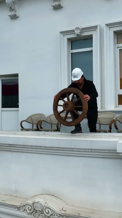 Prezentatorul examinează un ornament circular lângă ferestrele fațadei.