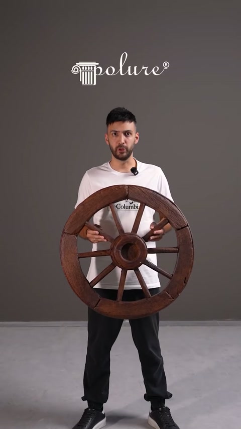 Prezentatorul expune o roată decorativă maro cu aspect rustic.