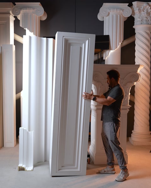 Un muncitor transportă un profil vertical lung prin atelier.