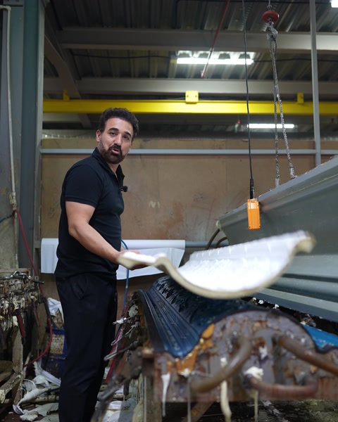 Bărbat ține un profil curbat lângă macaraua din hala de producție.