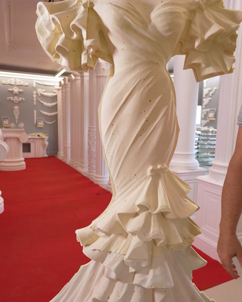 Coloană sculptată în formă de rochie de mireasă, așezată pe covor roșu
